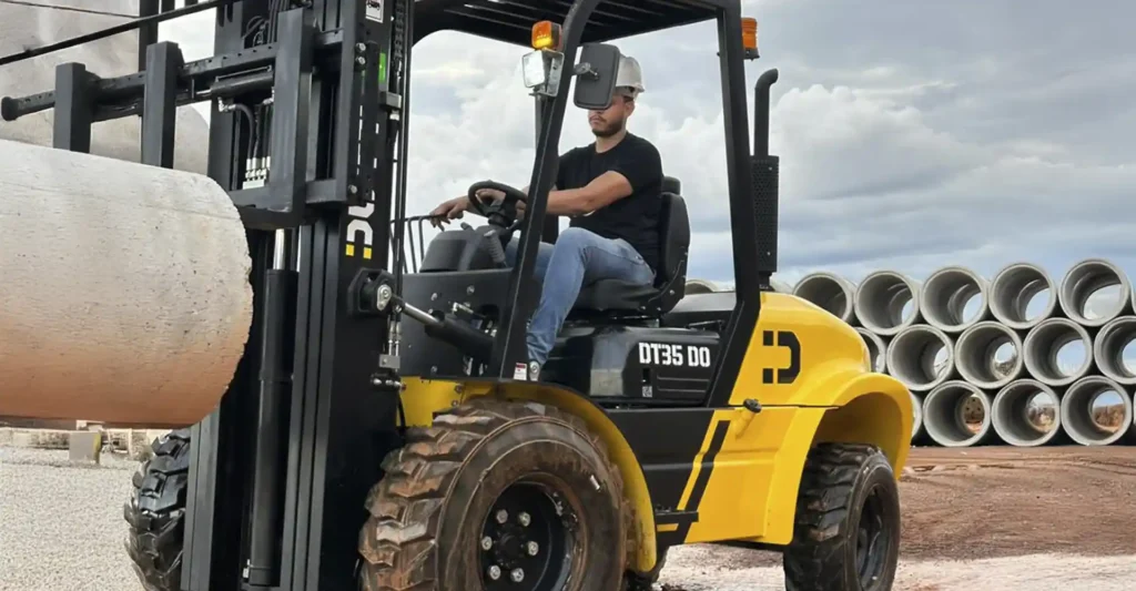 Empilhadeira Off-Road Dutt DT35 DO transportando tubos de concreto em canteiro de obras, destacando pneus de alta tração e design para terrenos irregulares