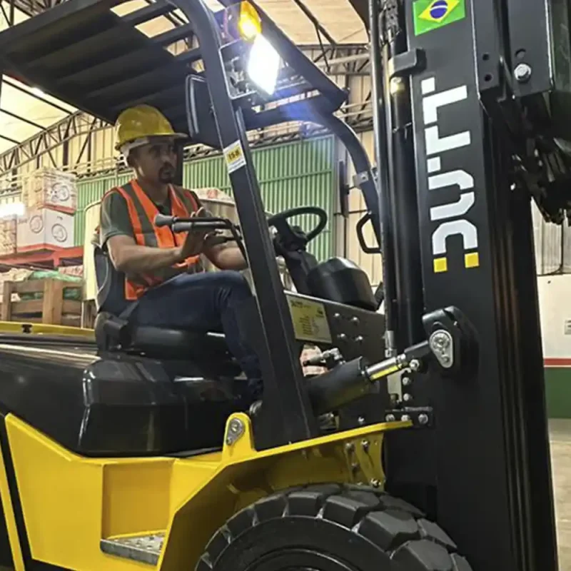 Empilhadeira a combustão Dutt DT35D amarela em operação dentro de armazém, transportando pallet de madeira em estantes metálicas de alta capacidade.