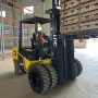 Vista frontal diagonal da empilhadeira Dutt DT35D com pneus duplos dianteiros, carregando pallet com bobinas metálicas em galpão logístico moderno