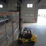 Visão superior de empilhadeira Dutt DT35D posicionando mercadoria no nível superior de estrutura de armazenagem, destacando o teto de proteção do operador