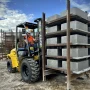 Empilhadeira todo terreno Dutt DT35 DO operando em pátio de fábrica de artefatos de cimento, carregando pallets de blocos sobre solo de terra batida