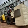 Empilhadeira Off-Road Dutt DT35 DO utilizando acessório clamp para transportar fardos de algodão ou fibra em área externa industrial com silos metálicos